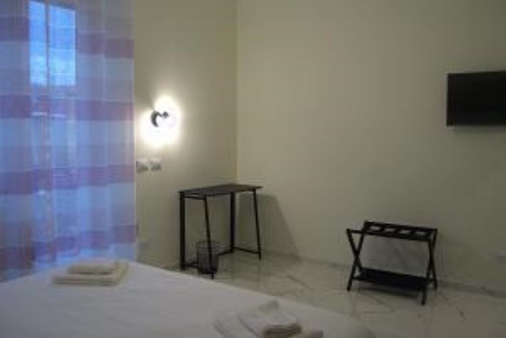 Et hotelværelse med seng, lille bord, tv på væggen og et vindue med gardiner.