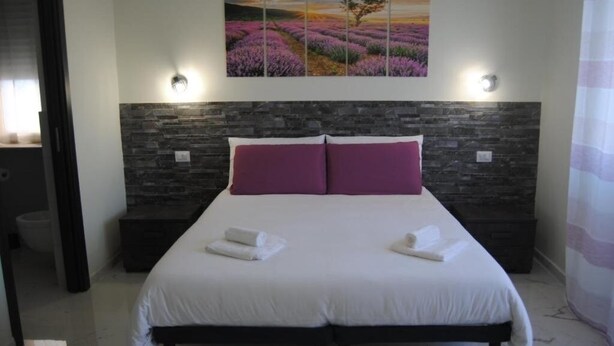 Une chambre avec un grand lit, deux tables de chevet, un mur en pierre et un tableau représentant des champs de lavande.