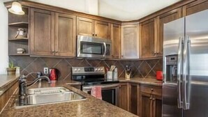 A kitchen with wooden cabinets, a stainless steel refrigerator, a microwave, and a granite countertop.