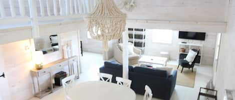 A spacious living area with a white dining table, blue sofa, and a hanging light fixture.