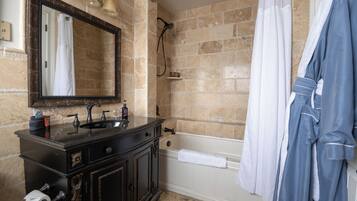 A bathroom with a dark wooden vanity, a large mirror, a bathtub, and a blue robe hanging on the wall.
