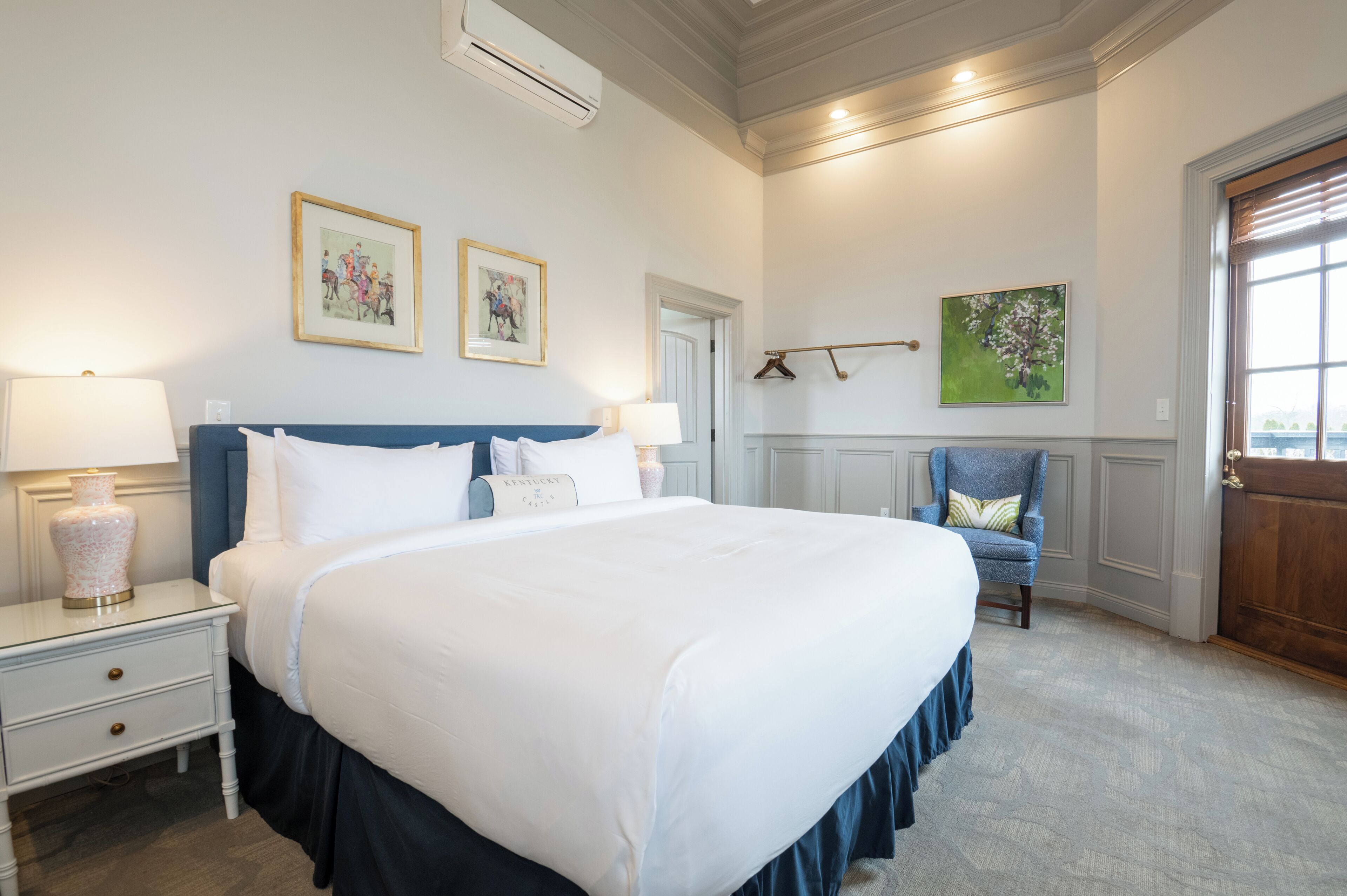 A neatly arranged bedroom with a large bed, bedside lamps, a chair, and artwork on the walls.