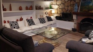 Een woonkamer met een stenen muur, een open haard, een zithoek en planken met decoratieve objecten.