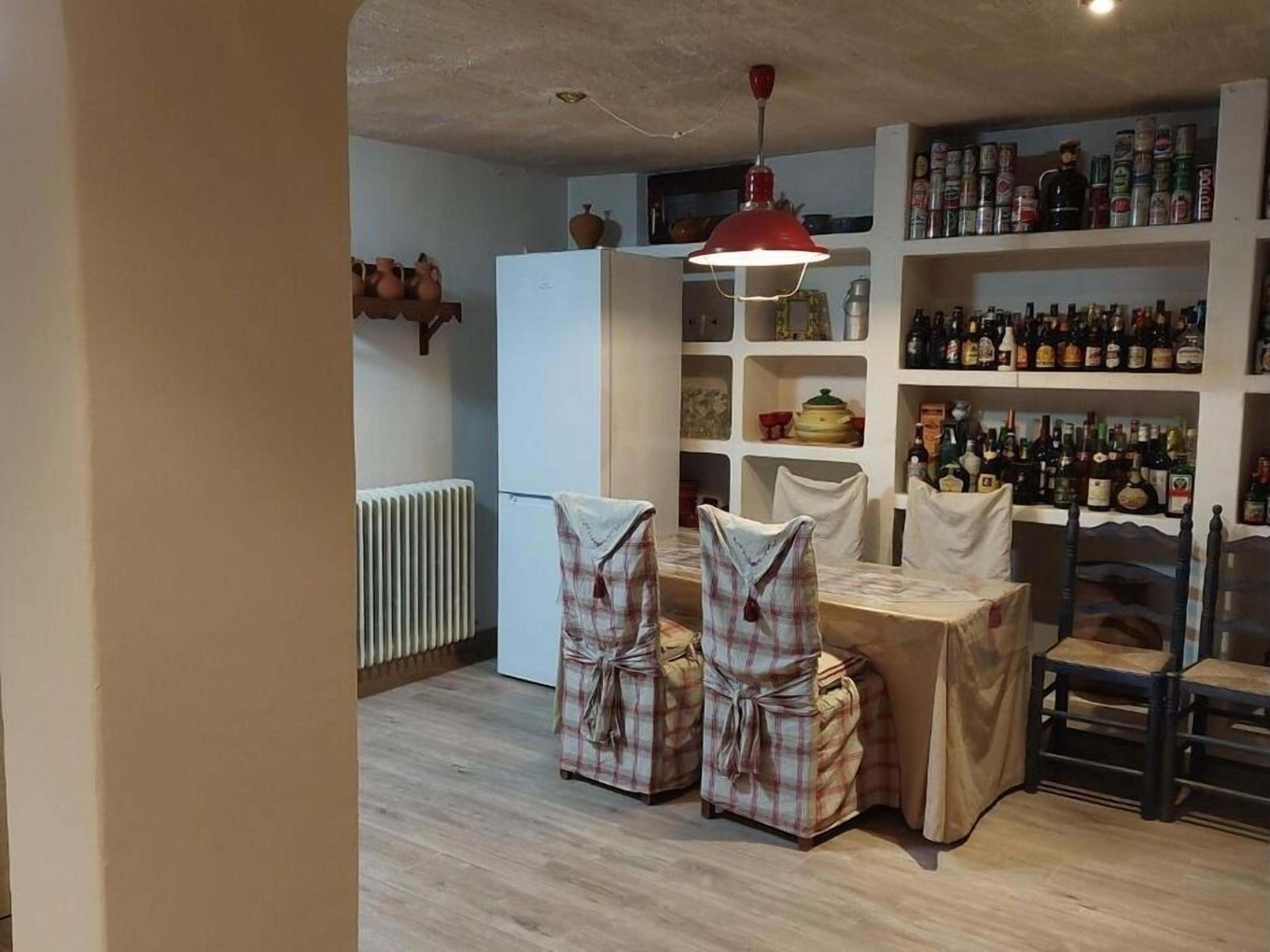 Ein Essbereich mit Tisch und Stühlen, die mit karierten Tischdecken bedeckt sind, einer roten Pendelleuchte und Regalen voller Flaschen und Gläser.