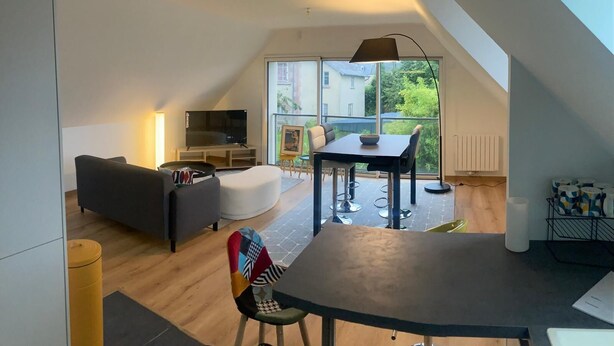 Um apartamento loft moderno com área de jantar, sofá, televisão e varanda com vista para o bairro.