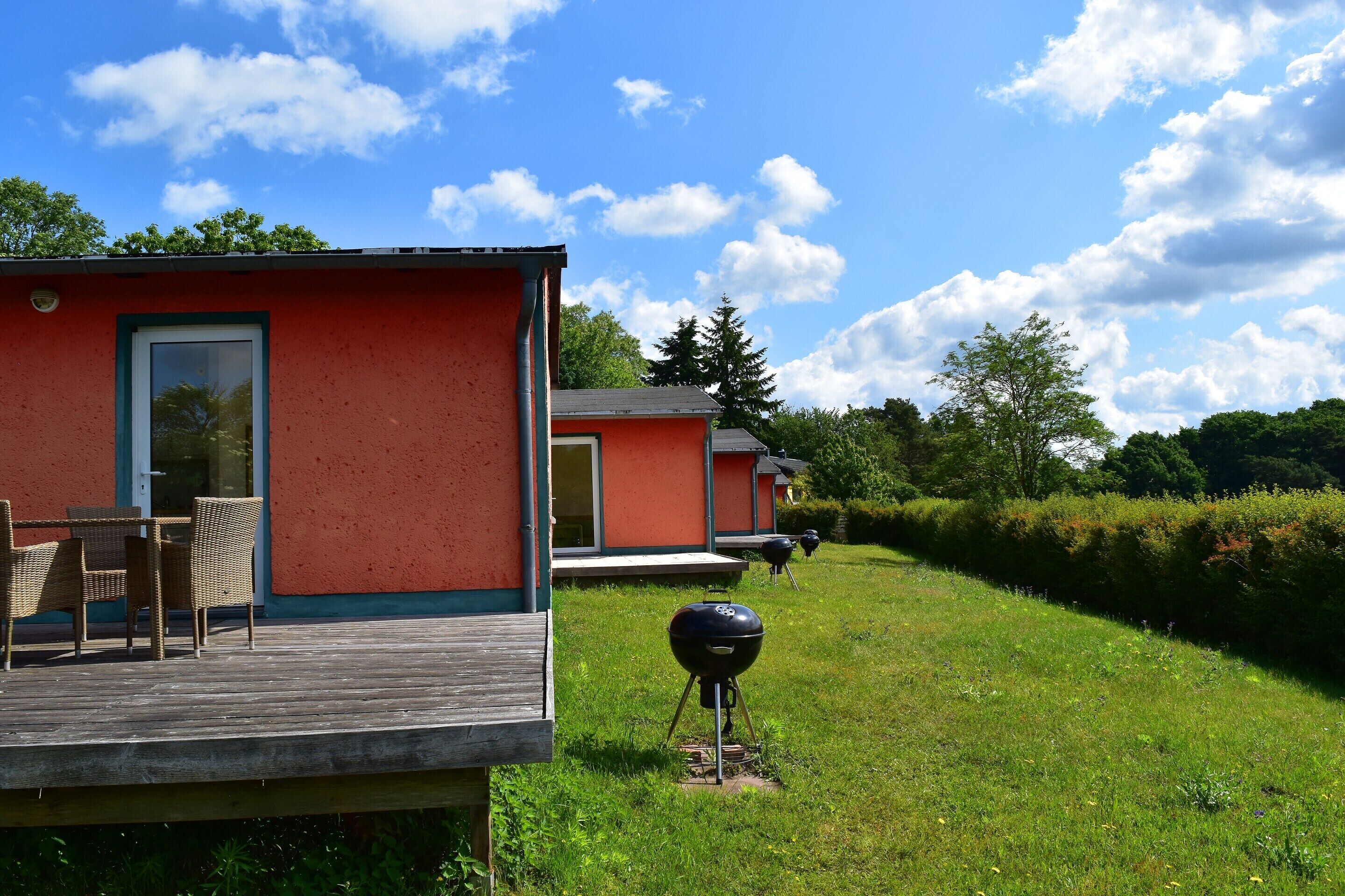 A red building with a deck and outdoor seating, surrounded by a grassy area and trees.