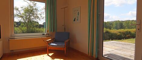 Ein Zimmer mit Holzboden, einem Sessel, einem Heizkörper, einem Fenster und einer Tür, die nach draußen führt.