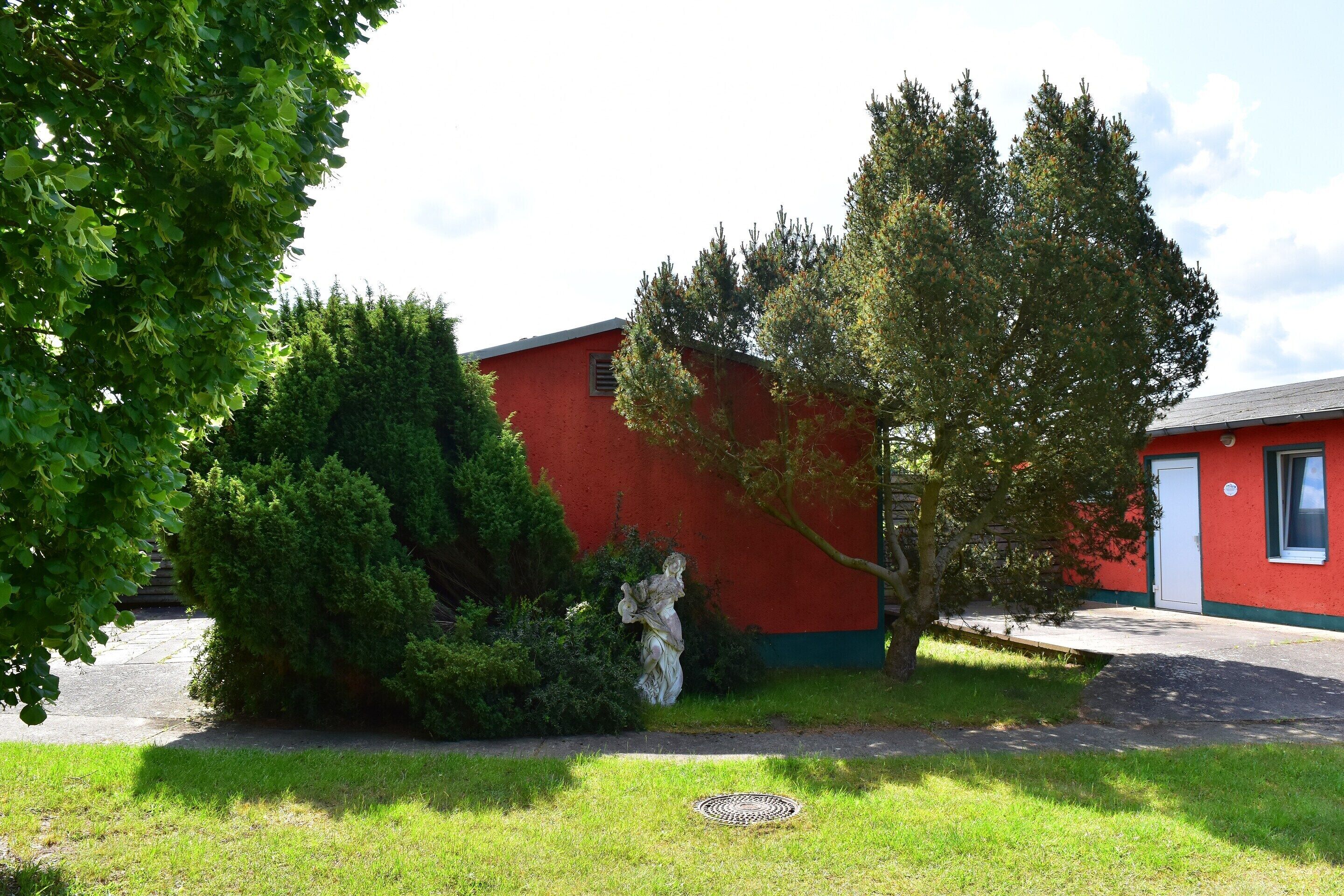 A red building with a white door, surrounded by green grass and trees.