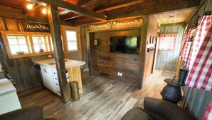 L’intérieur d’un chalet rustique est doté d’un plancher en bois, d’un coin cuisine avec un évier et des placards, d’un téléviseur fixé au mur et d’un espace salon avec deux fauteuils.