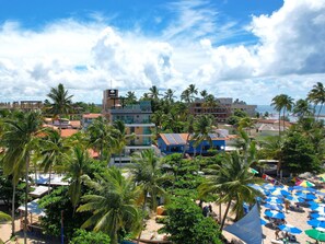 A beachside hotel with multiple floors, palm trees, and beach umbrellas. - TEKATETU Hotels&Flats - Makadamia (Ipojuca)