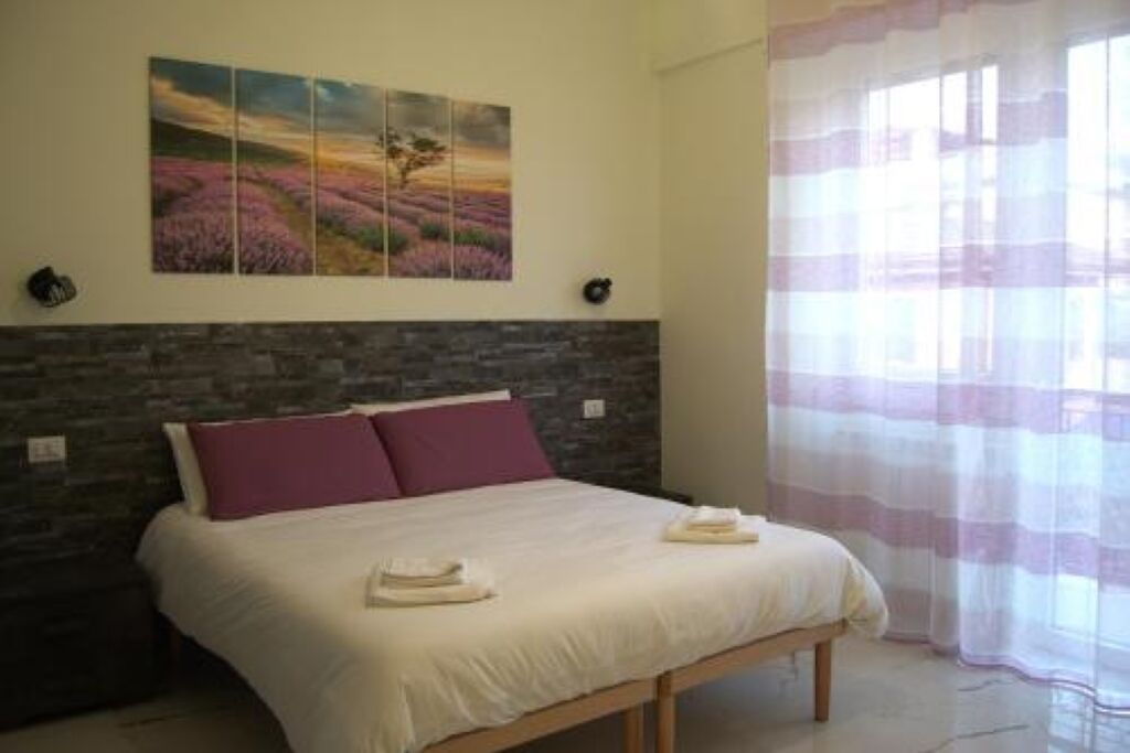 Une chambre à coucher avec un lit, un mur en pierre, un tableau et une fenêtre ornée de rideaux légers.
