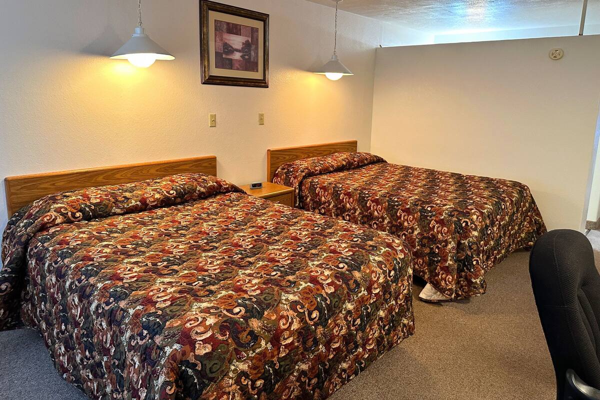 A hotel room with two beds, each with a patterned bedspread, a small bedside table, and a wall-mounted picture.
