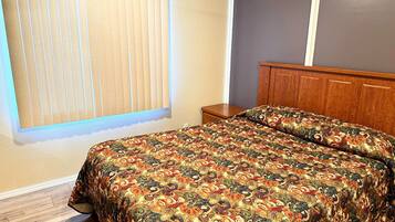 A bedroom with a bed, a nightstand, a window with blinds, and a wooden headboard.