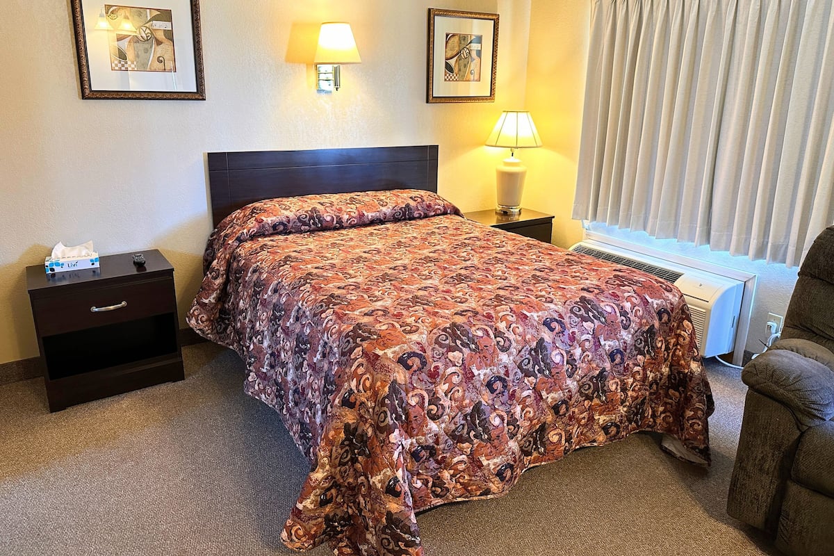 A hotel room with a bed, bedside tables, a lamp, a heater, and curtains.