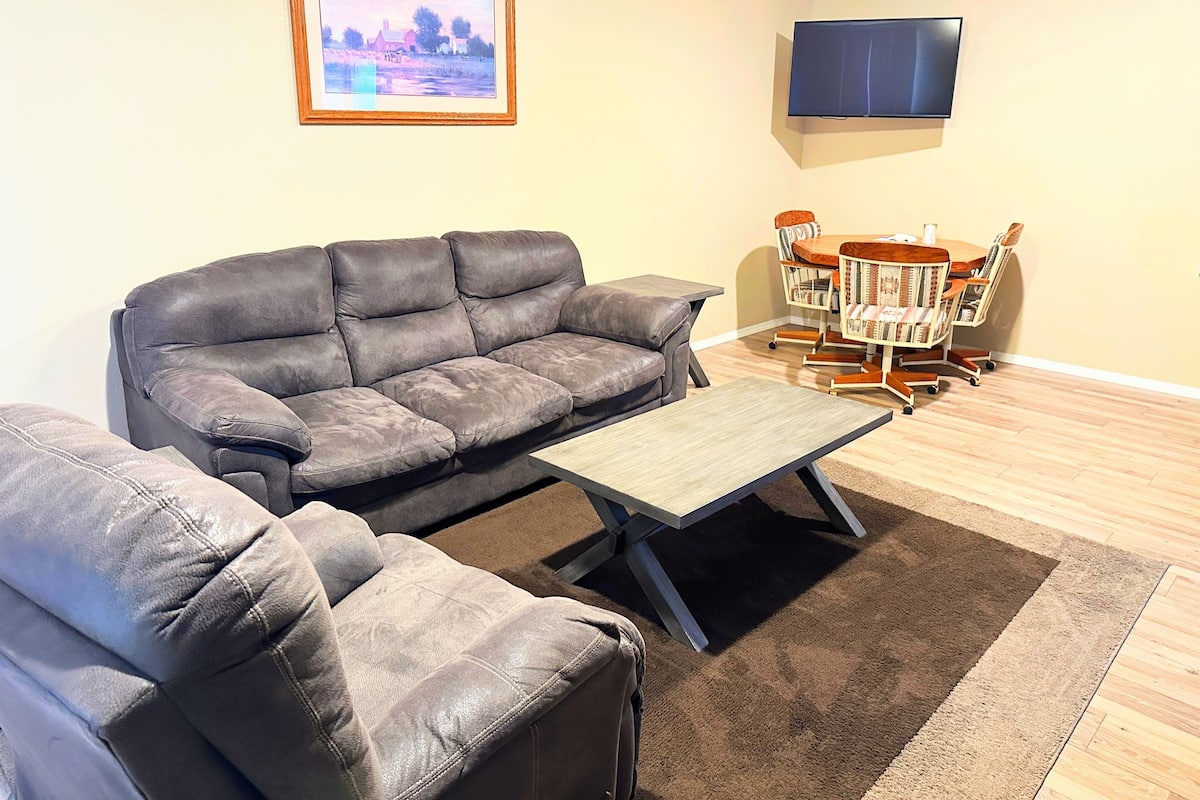 A living room with a grey sofa, a wooden coffee table, and a dining table with chairs.