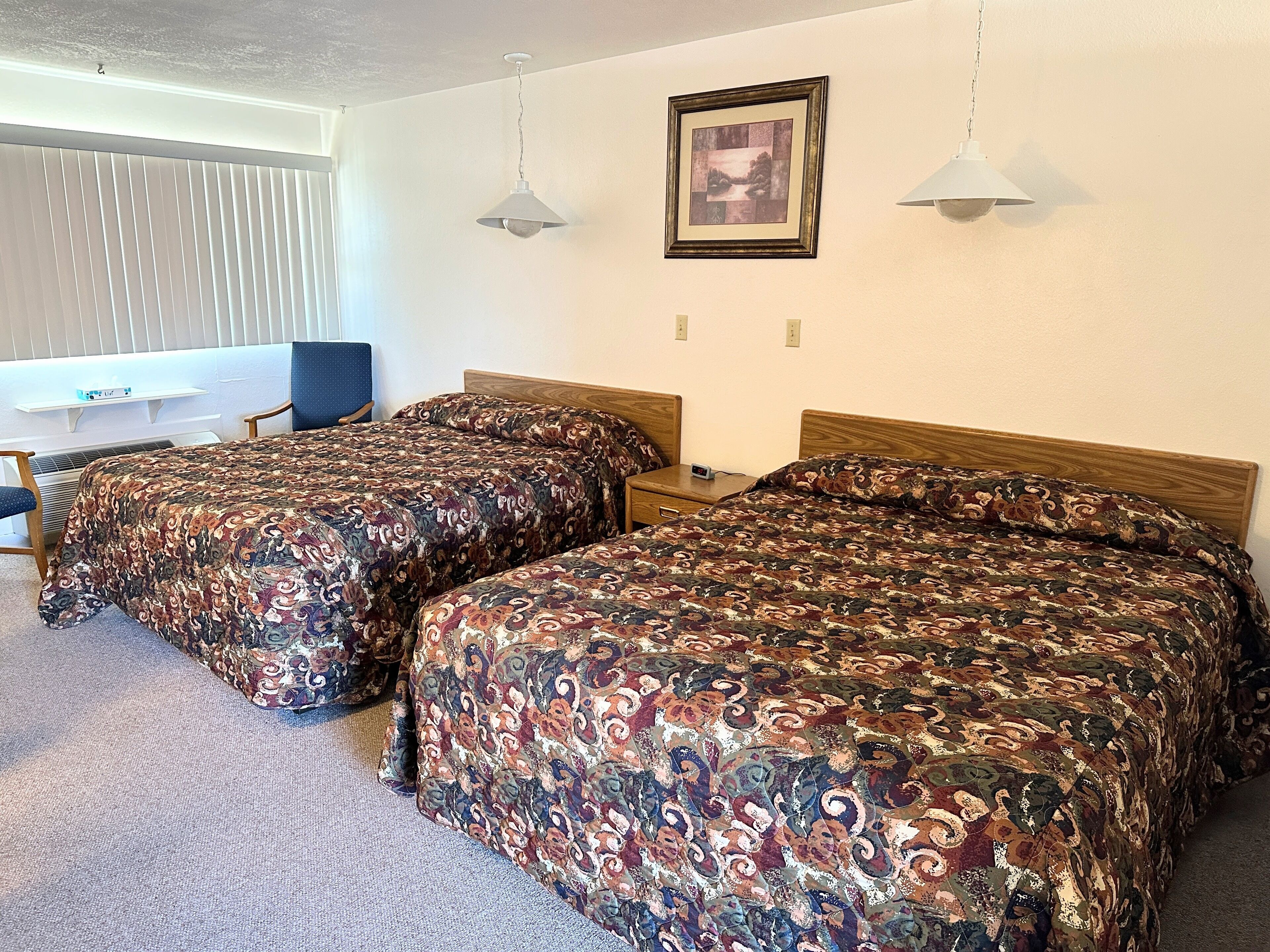 A hotel room with two beds, a desk, and a chair.