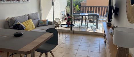A living room with a sofa, a dining table, chairs, a fan, and a view of the outdoors.