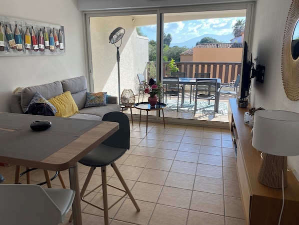 A living room with a sofa, a dining table, chairs, a fan, and a view of the outdoors.