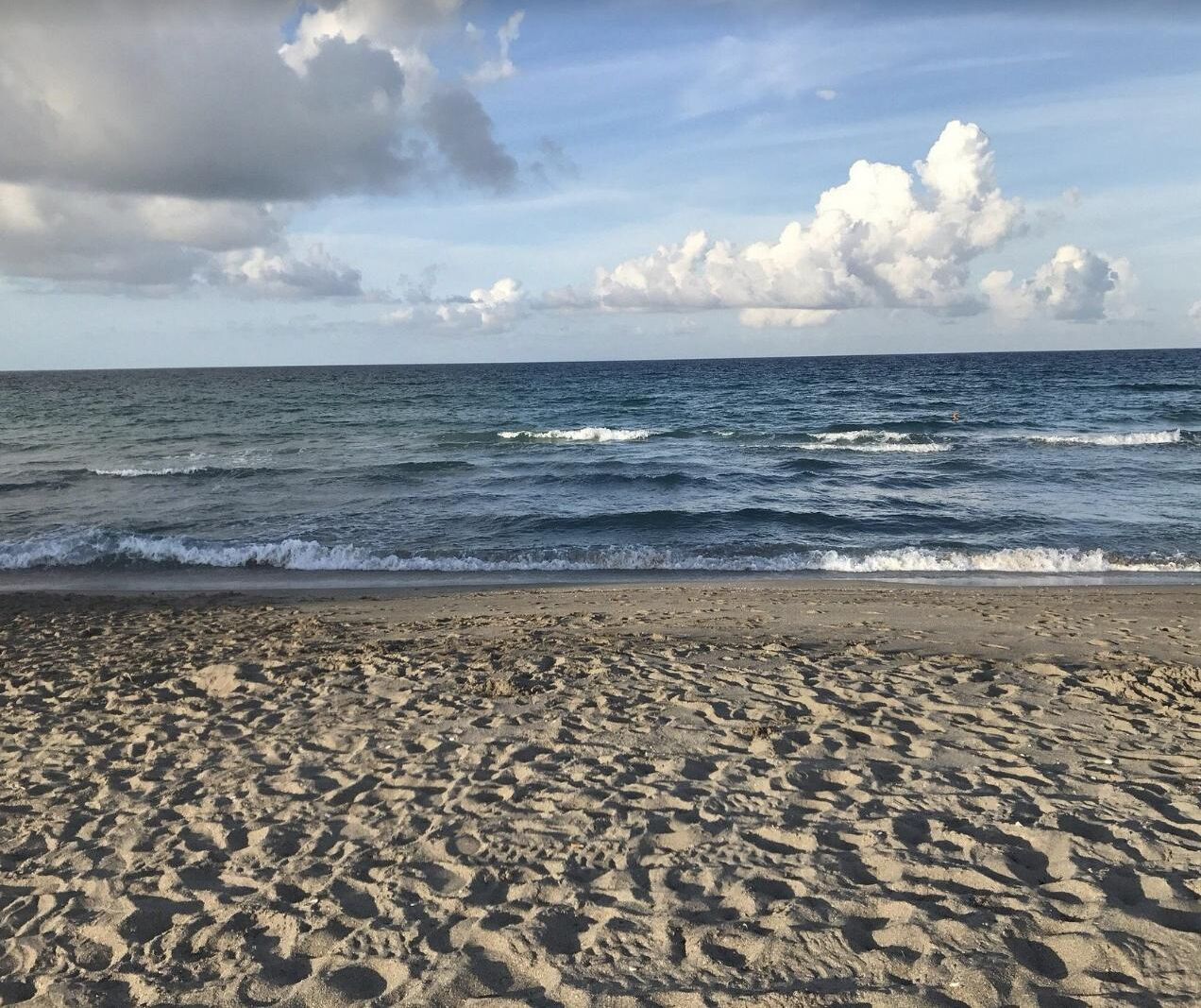 A sandy beach with waves approaching the shore under a partly cloudy sky.