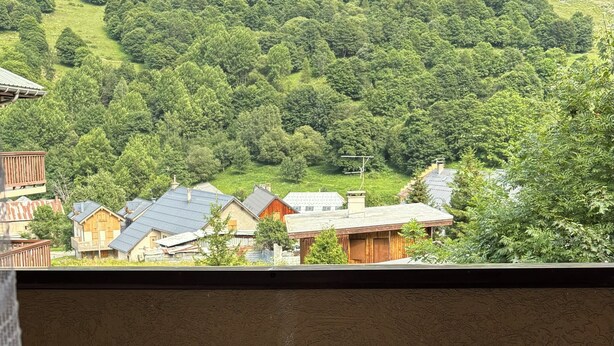 En balkon med et lille rundt bord og to stole, med udsigt over en grøn bakke med huse.