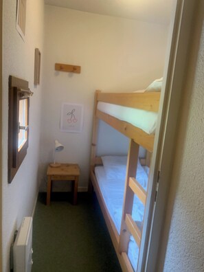 A narrow room with a bunk bed, a small table with a lamp, a radiator, and a framed picture on the wall. - Apartment in Valloire at the foot of the slopes (Valloire)