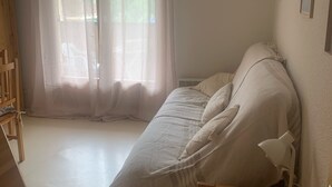 Et soveværelse med en seng, et træbord, en stol og et vindue med lette gardiner.