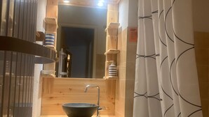 Et badeværelse i træ med et stort spejl, en skålhåndvask og et bruseforhæng med et geometrisk mønster.