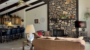Ein geräumiger Wohnbereich mit Kamin aus Stein, einer Couch und einem Essbereich mit Barhocker.