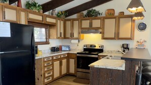 Eine Küche mit Holzausstattung, einem schwarzen Kühlschrank, einem Herd und einem Spülbecken.