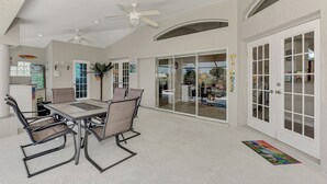Ein großzügiger Patio-Bereich mit Esstisch und Stühlen, Deckenventilatoren und einer Glastür zum Garten.