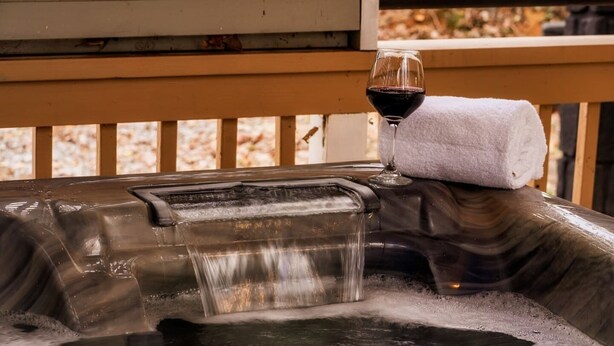 A hot tub with a waterfall feature and a glass of red wine on a towel. - Outlander Couples Cottage/Walk to Downtown/Hot Tub (Gatlinburg)