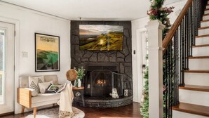 A living room with a stone fireplace, a sofa, a coffee table, and a framed landscape painting. - Outlander Couples Cottage/Walk to Downtown/Hot Tub (Gatlinburg)