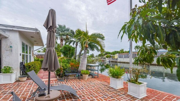 An outdoor patio with brick flooring, a covered table with chairs, and a small pool.