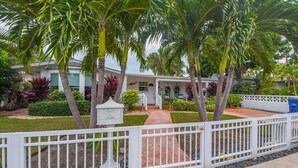 A house with a white fence, palm trees, and a pathway leading to the entrance.