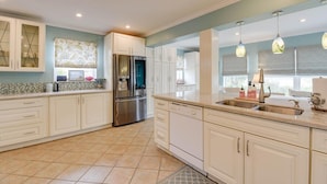 A modern kitchen with white cabinetry, a stainless steel refrigerator, and a large island with a sink.