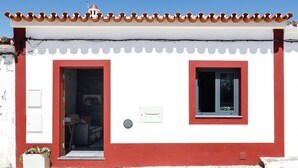 Un edificio blanco con detalles en rojo y techo de tejas. Se ve una puerta y una ventana.