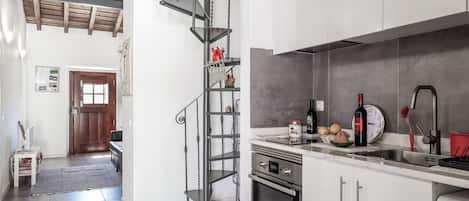 A modern kitchen with white cabinets, stainless steel appliances, and a spiral staircase.