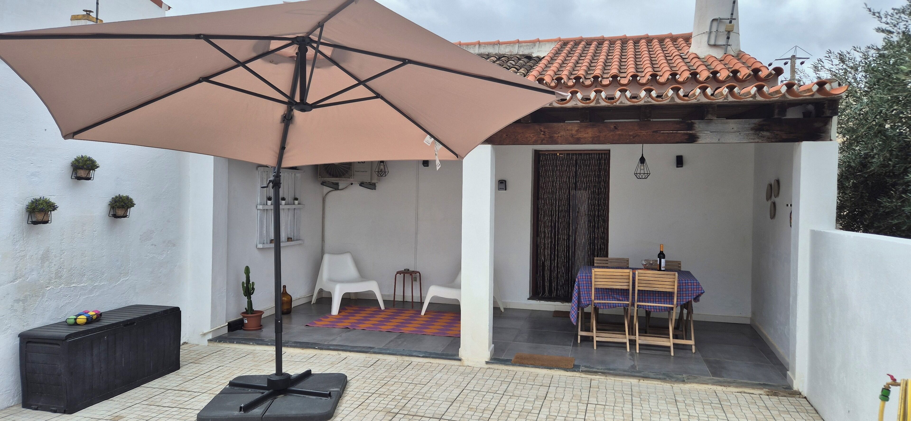 Un patio con mesa y sillas, un paraguas grande y plantas en macetas.