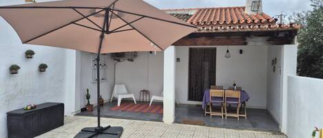 Un patio con mesa y sillas, un paraguas grande y plantas en macetas.