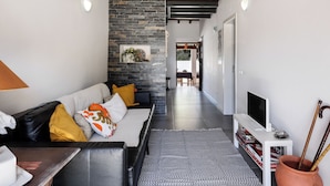 Una sala moderna con una pared de acento de piedra, un sofá de cuero negro y un televisor de pantalla plana sobre un mueble blanco.