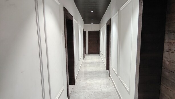 A long, narrow hallway with white walls and a marble floor, leading to a dark wooden door at the end. - Serendipity by the Ganges (Varanasi)
