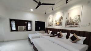A hotel room with two beds, a ceiling fan, wall-mounted air conditioning, and artwork. - Serendipity by the Ganges (Varanasi)