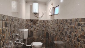A bathroom with a toilet, a shower, and a water heater. The walls are tiled with a geometric pattern. - Serendipity by the Ganges (Varanasi)