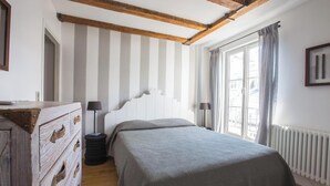 A bedroom with a wooden ceiling, a bed with a striped bedspread, a dresser, a radiator, and a window with curtains. - LOCATED IN ONE OF PARIS’S MOST ICONIC NEIGHBORHOODS SAINT GERMAIN - RUE DRAGON  (Paris)