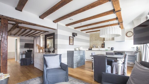 A modern living room with exposed wooden beams, a striped wall, and a kitchen in the background. - LOCATED IN ONE OF PARIS’S MOST ICONIC NEIGHBORHOODS SAINT GERMAIN - RUE DRAGON  (Paris)
