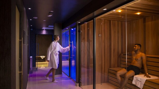 Et moderne spaområde med en træsauna og et massageværelse med glasvægge.