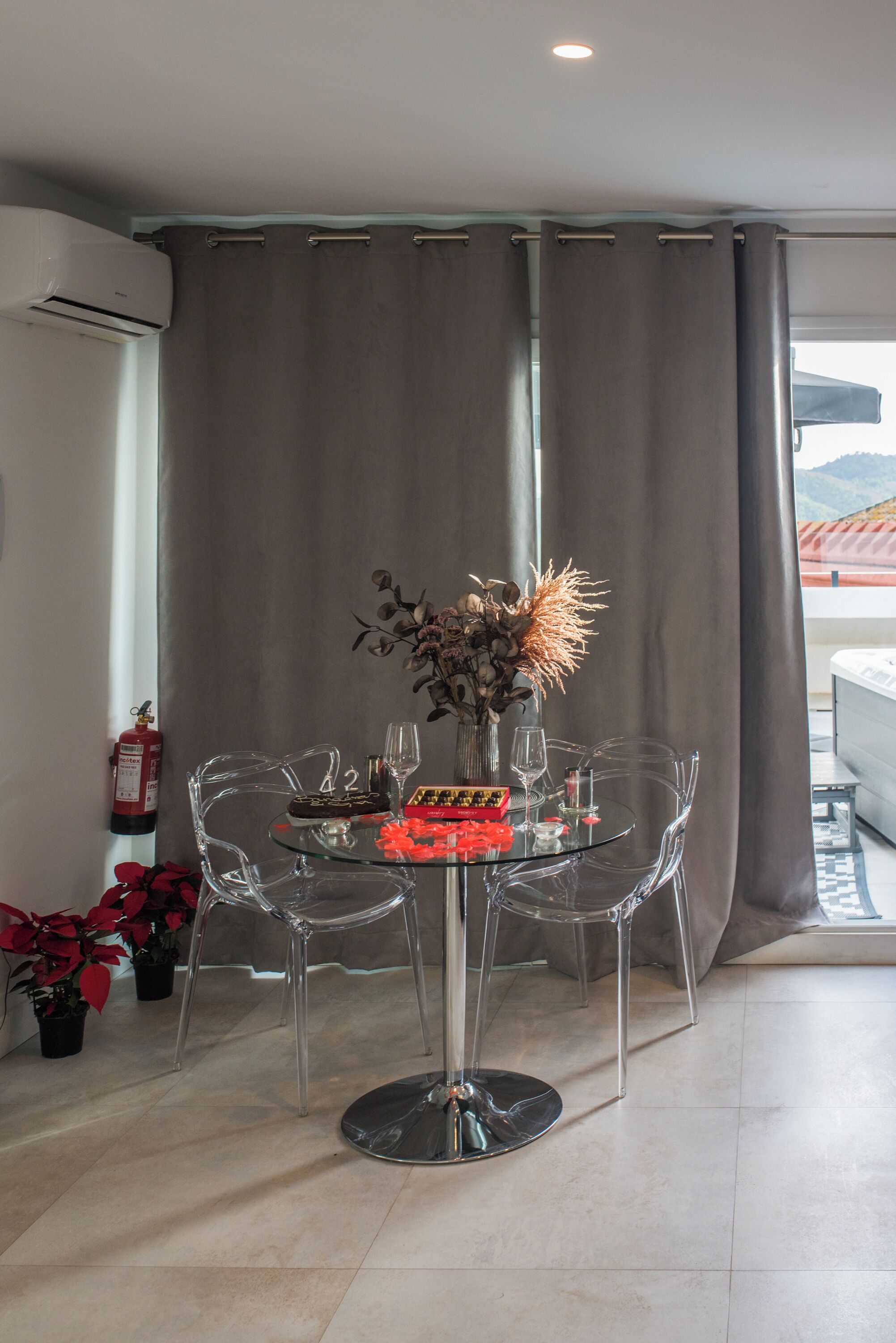 A modern dining area with a glass table, clear chairs, and a vase with dried flowers.