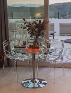 A glass-top table with chairs, a vase with dried flowers, and a bottle of wine.