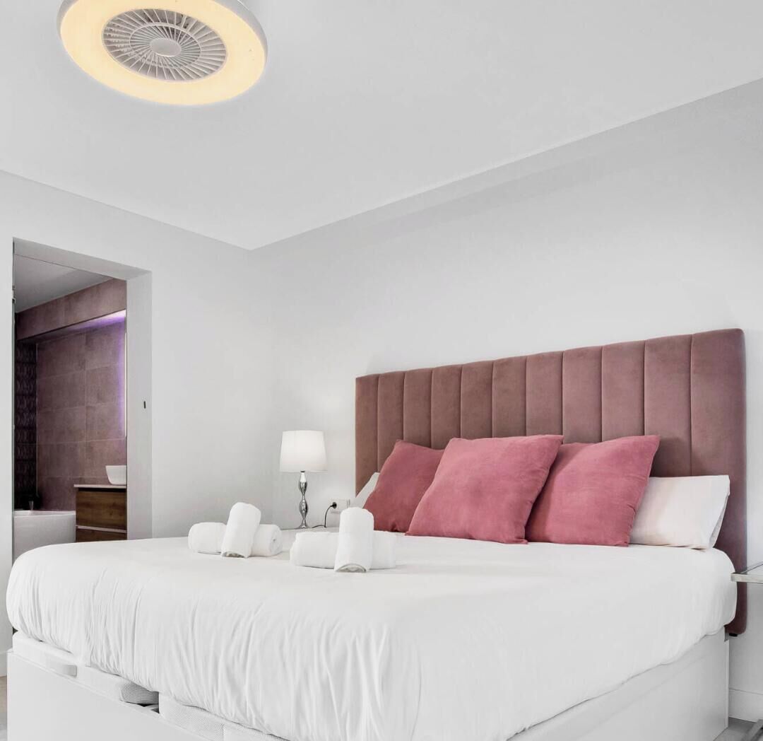 Ein modernes Schlafzimmer mit einem großen Bett, einem Kopfteil und einem Nachttisch mit Lampe.