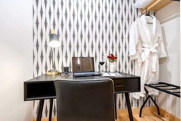 Une pièce comprenant un bureau, un ordinateur portable, une lampe, un vase avec des fleurs et un peignoir suspendu à un porte-manteau.